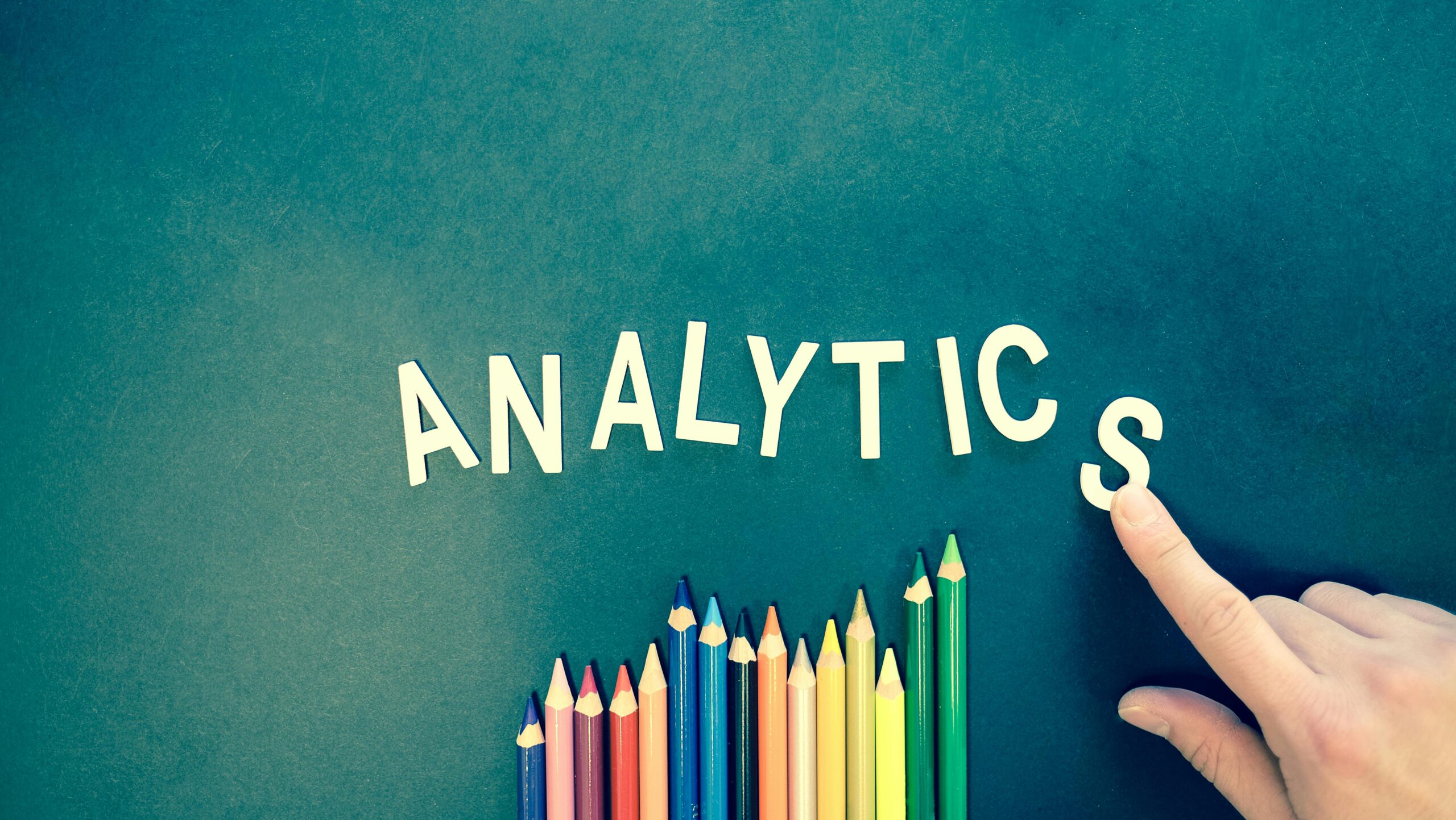 The word “analytics” is written on a green background with color pencils kept at the bottom. 